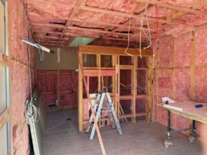 Inside a room on a construction site showing wall framing and insulation. There are tools and a ladder. 