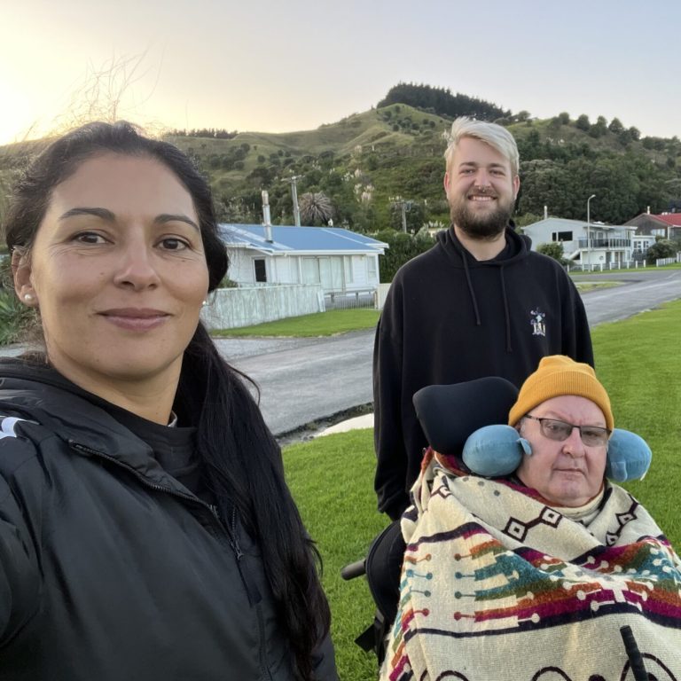 Tania, Dean, and Pete pose for a selfie. They are at a viewing point to watch a Rocket Lab rocket launch together.