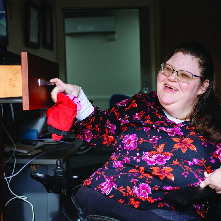 A person who uses a wheelchair is smiling and putting away their laundry in their bedroom.