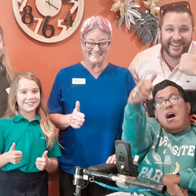 A group of smiling people including a nurse, a wheelchair user, a child and parent, and Enliven Disability Service Manager, Andrew Wordsworth. The group are giving a thumbs up signal with their hands.